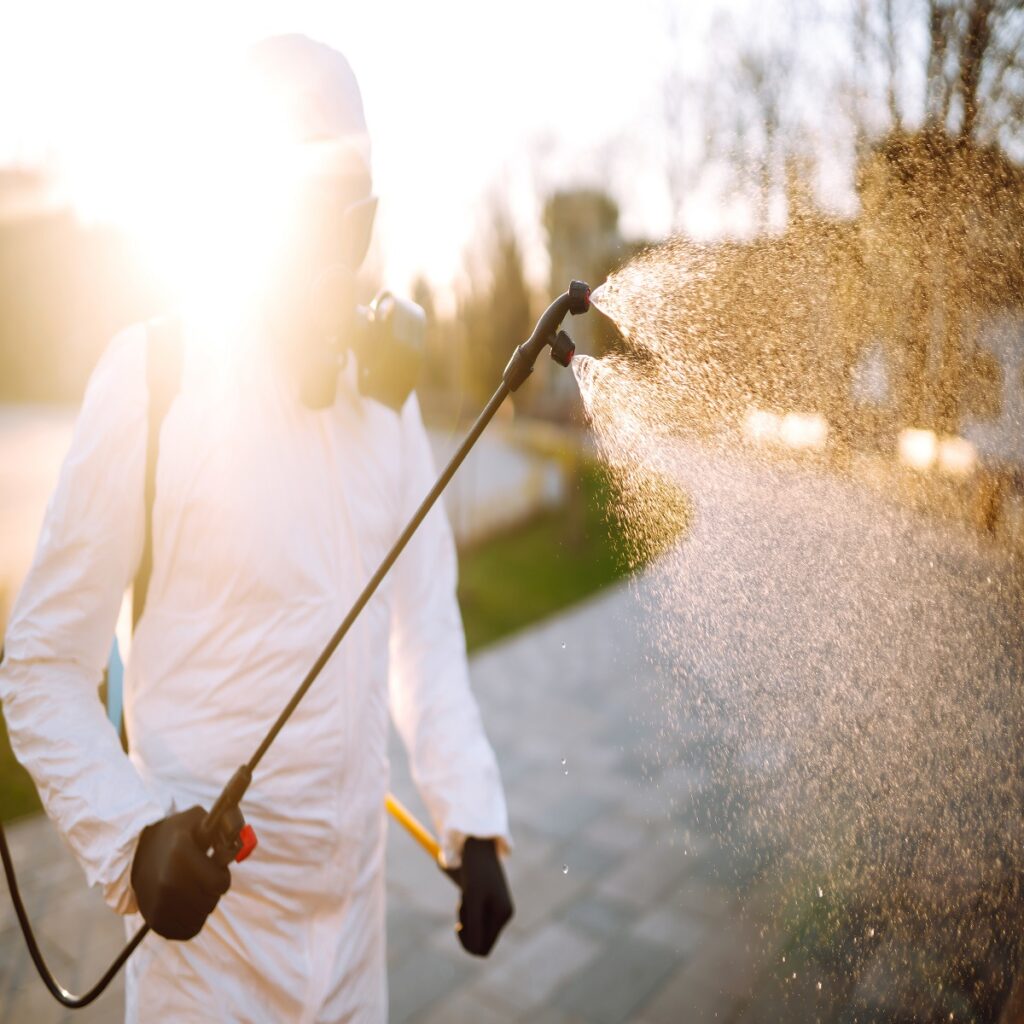 Man wearing protective suit disinfecting public places in the sun with spray chemicals to preventing the spread of coronavirus, pandemic in quarantine city. Covid -19. Cleaning concept.